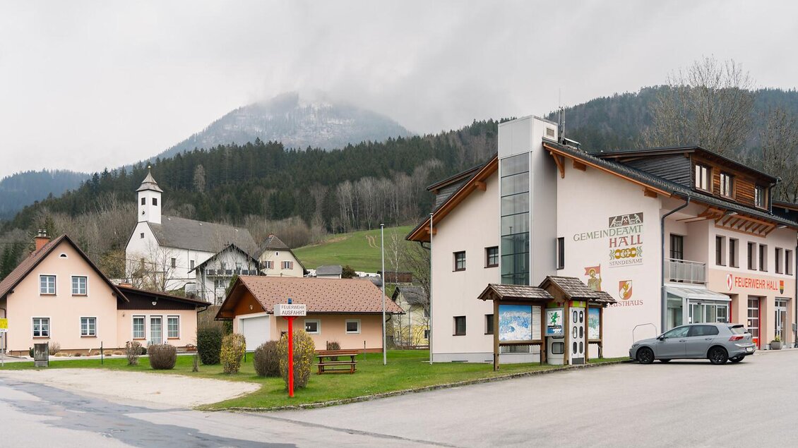 Eine malerische Dorfansicht mit charmanten Gebäuden und einem kleinen Kirchturm. Im Hintergrund sind bewaldete Hügel und bewölkter Himmel zu sehen. | © Christoph Lukas