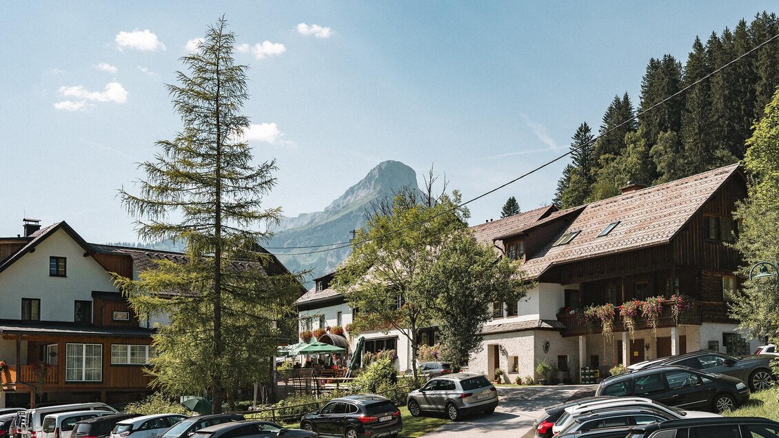 Ein malerisches Dorf mit traditionellen Häusern und malerischer Bergkulisse. Parkplätze und Bäume schaffen eine einladende Atmosphäre.