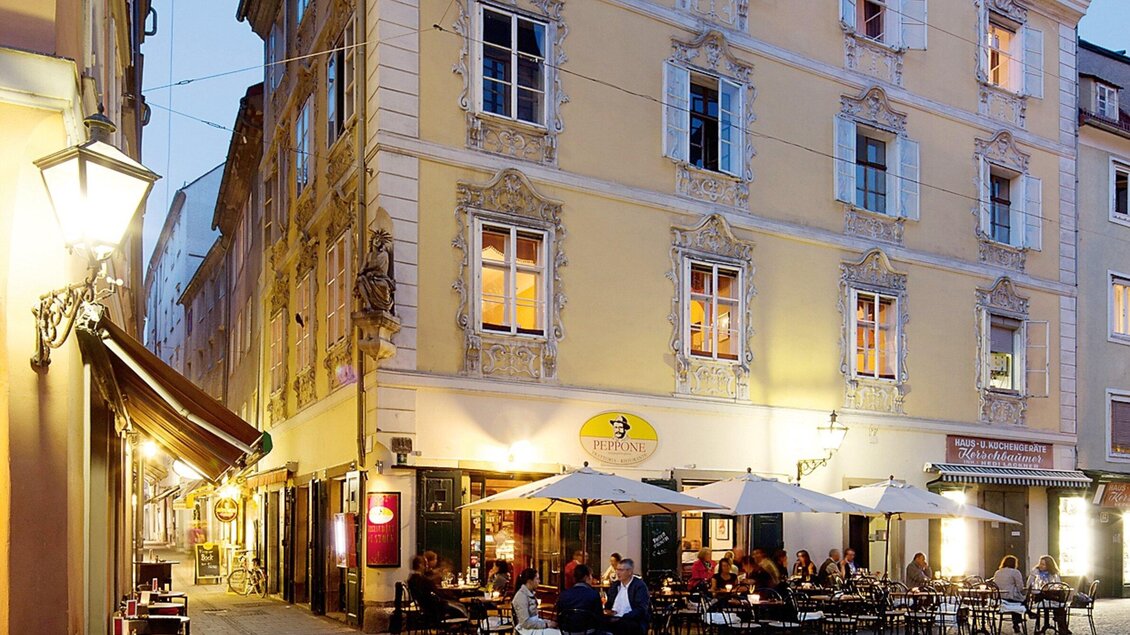 Ein einladendes Straßencafé in einer geschäftigen Gasse. Die bunten Tische unter den Schirmen laden zum Verweilen ein. | © CMS