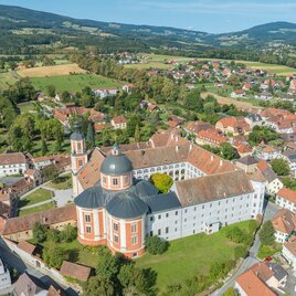 Eine beeindruckende Klosteranlage mit einem großen Garten, umgeben von sanften Hügeln und kleinen Häusern. Die grüne Landschaft und der klare Himmel verleihen der Szenerie eine ruhige Atmosphäre. | © Helmut Schweighofer