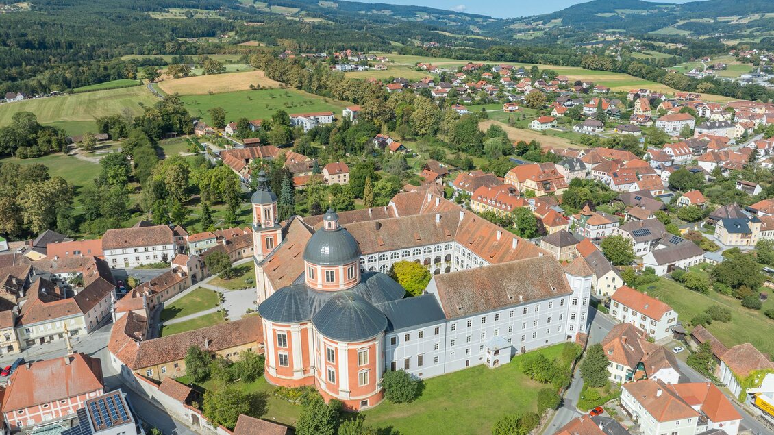 Eine beeindruckende Klosteranlage mit einem großen Garten, umgeben von sanften Hügeln und kleinen Häusern. Die grüne Landschaft und der klare Himmel verleihen der Szenerie eine ruhige Atmosphäre. | © Helmut Schweighofer