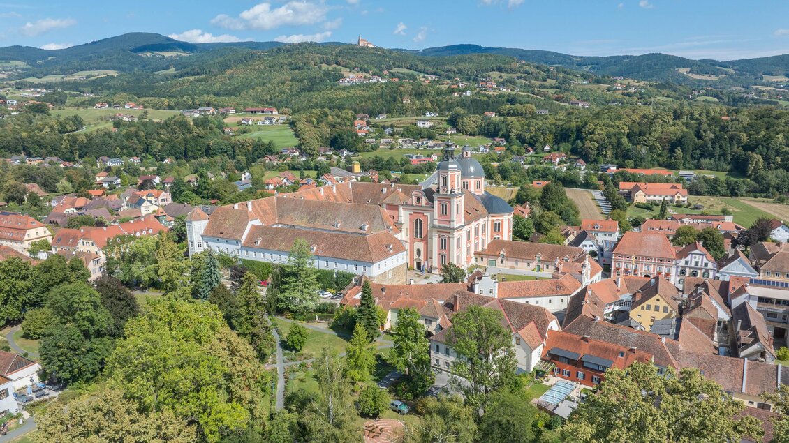 Eine malerische Landschaft mit einer historischen Kirche im Zentrum. Umgeben von grünen Hügeln und kleinen Häusern bietet die Umgebung einen ruhigen Blick auf die Natur. | © Helmut Schweighofer