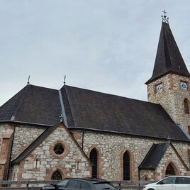 An old stone church with a tall tower. Surrounded by trees and some cars in the foreground. | © Stephanie Bor