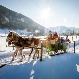 A sled ride through a wintry landscape with snow and mountains in the background. The sun is shining brightly, creating a lovely atmosphere. | © Tourismusverband Murau