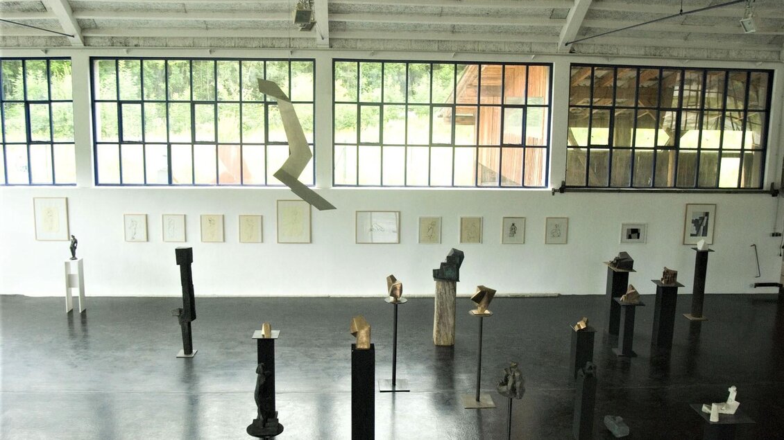 Ein heller Ausstellungsraum mit großen Fenstern. Mehrere Skulpturen stehen auf Podesten, und an der Wand hängen Zeichnungen. | © Pillhofer