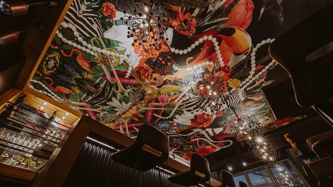 Ein stilvolles Restaurant mit einer bunten, künstlerischen Decke und eleganten Beleuchtung. Die Einrichtung ist modern und einladend. | © Aiola - Joel Kernasenko