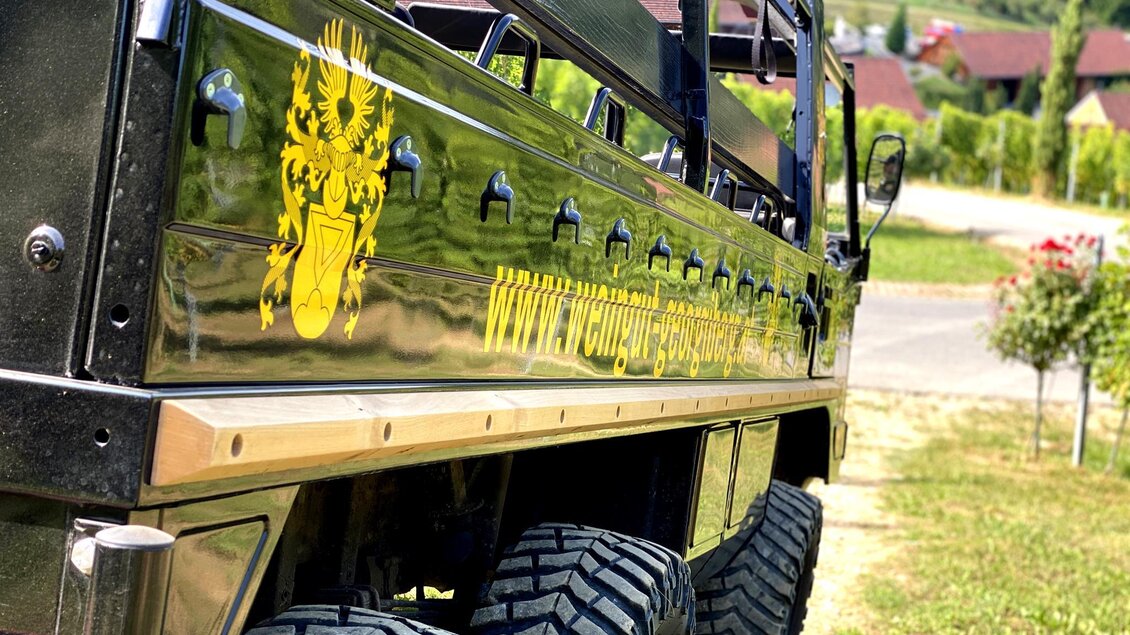 Ein robuster Geländewagen mit glänzender Oberfläche und auffälligem Emblem. Im Hintergrund sind sanfte Hügel und eine ländliche Landschaft sichtbar. | © Weingut Georgiberg