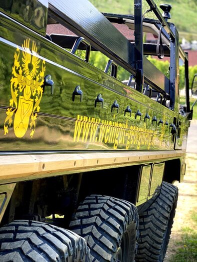 Ein robuster Geländewagen mit glänzender Oberfläche und auffälligem Emblem. Im Hintergrund sind sanfte Hügel und eine ländliche Landschaft sichtbar. | © Weingut Georgiberg