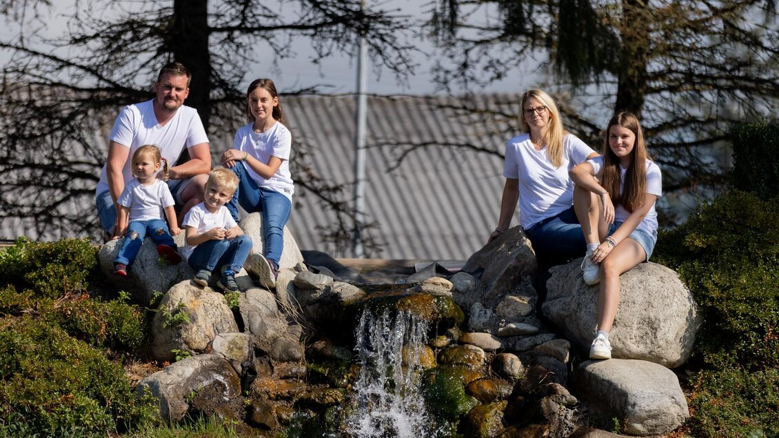 Eine fröhliche Familie sitzt an einem kleinen Wasserfall. Sie tragen lässige Kleidung und genießen die Zeit im Freien. | © Familie Lanz