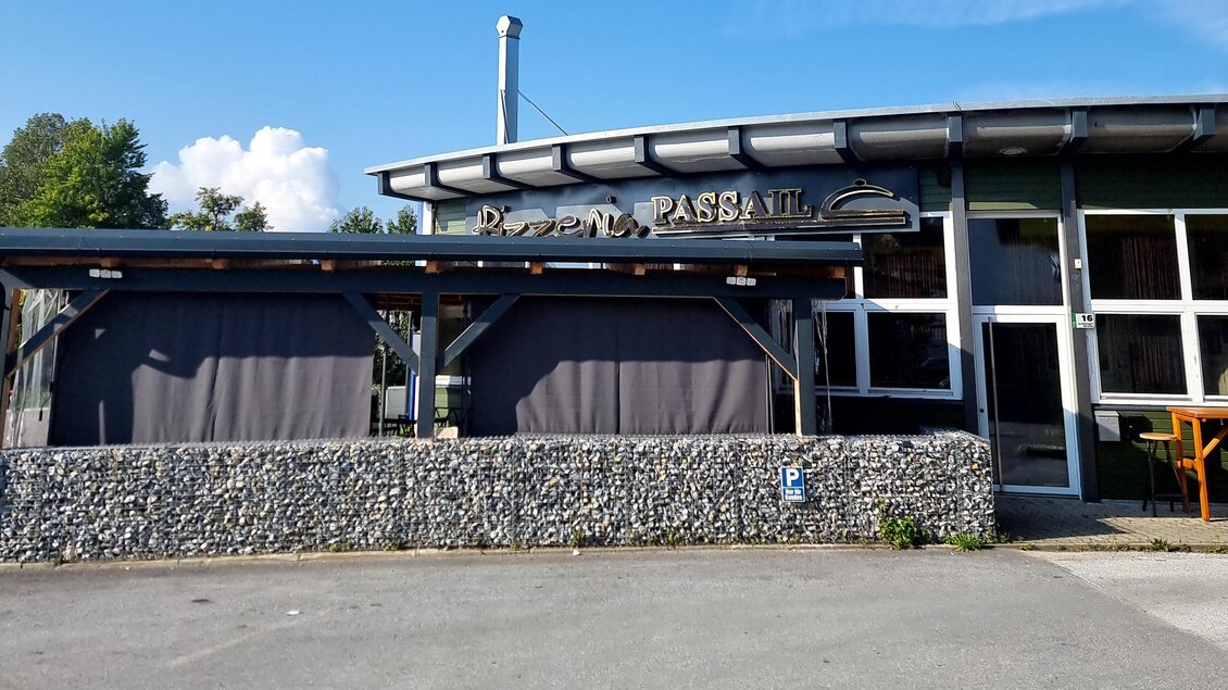 Ein modernes Restaurantgebäude mit einer großen Fensterfront. Es gibt einen überdachten Außenbereich mit grauen Vorhängen. | © Oststeiermark Tourismus