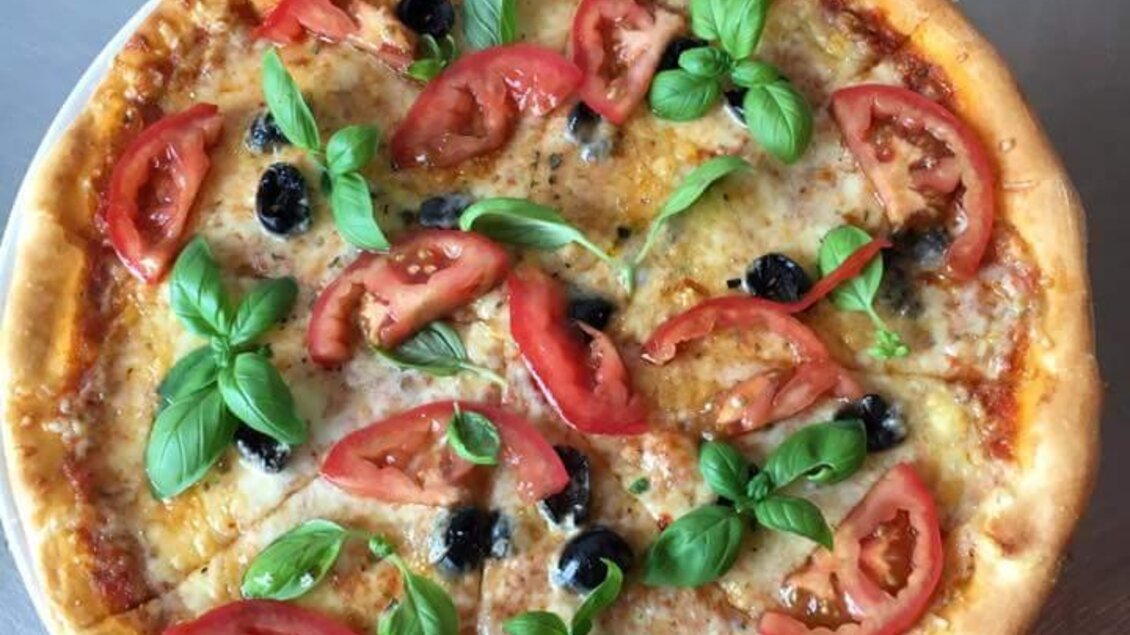 Eine frisch gebackene Pizza mit Tomaten, schwarzen Oliven und frischem Basilikum. Der Rand ist goldbraun und knusprig. | © Pizzeria Passail