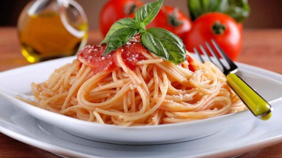 Ein Teller Spaghetti mit Tomatensauce, garniert mit frischem Basilikum. Im Hintergrund sind Olivenöl und frische Tomaten zu sehen. | © Pizzeria DAVID