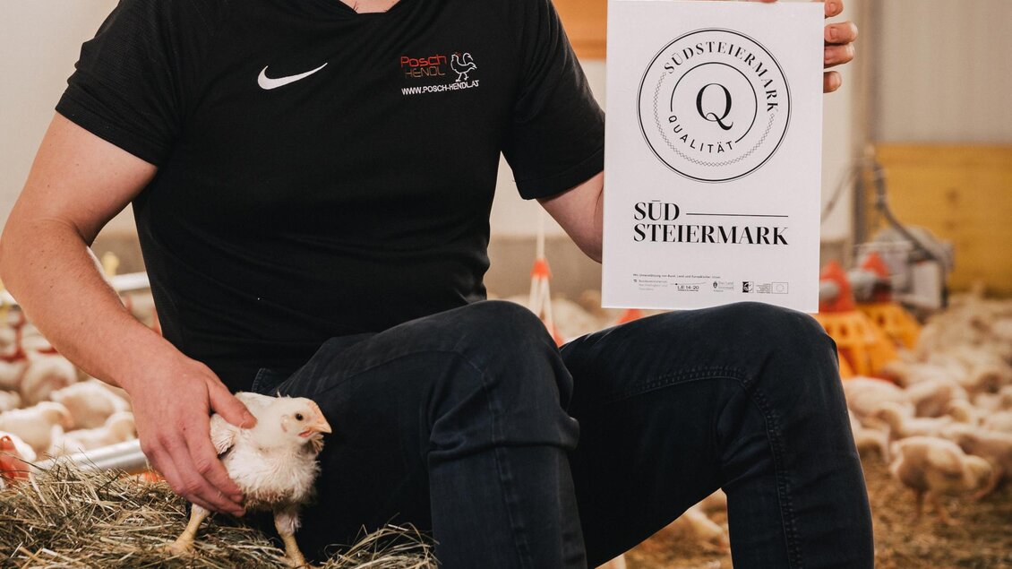 Ein junger Mann sitzt auf einem Heuballen und hält ein Schild in der Hand. Neben ihm befindet sich ein Meerschweinchen in einem Stall. | © RM SW GmbH | webquartier.at