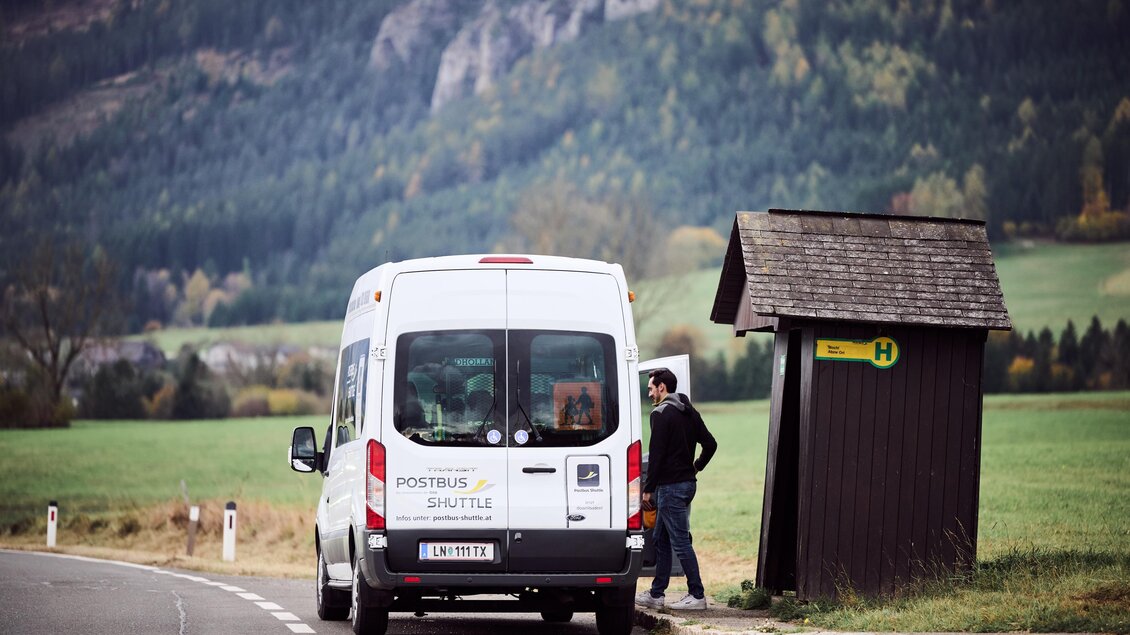 Ein Shuttlebus hält an einer Haltestelle in ländlicher Umgebung. Im Hintergrund sind üppige grüne Hügel und Wälder zu sehen. | © ÖBB/ Marek Knopp