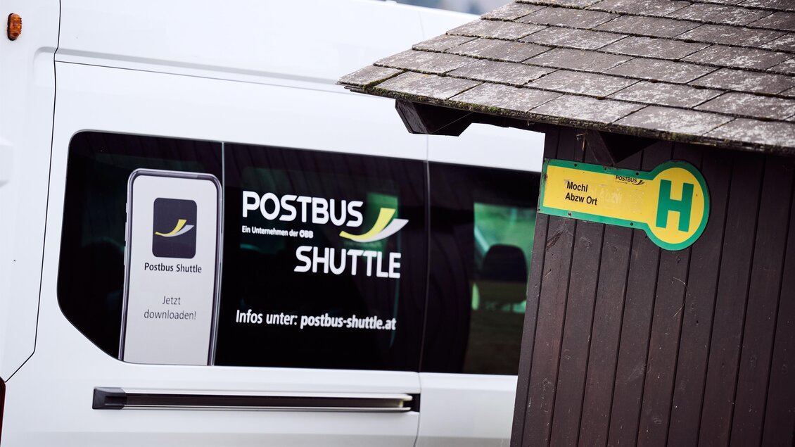 Ein Postbus Shuttle auf einer Haltestelle mit einem informativen Schild. Der Bus ist bereit für die Fahrgäste und bietet einen komfortablen Transportdienst an. | © ÖBB/ Marek Knopp