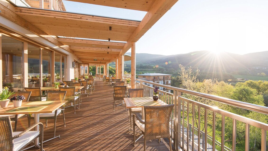 Eine helle Terrasse mit Holzmöbeln und Blick auf die hügelige Landschaft. Die Sonne scheint und verbreitet eine einladende Atmosphäre. | © RETTER Bio-Natur-Resort