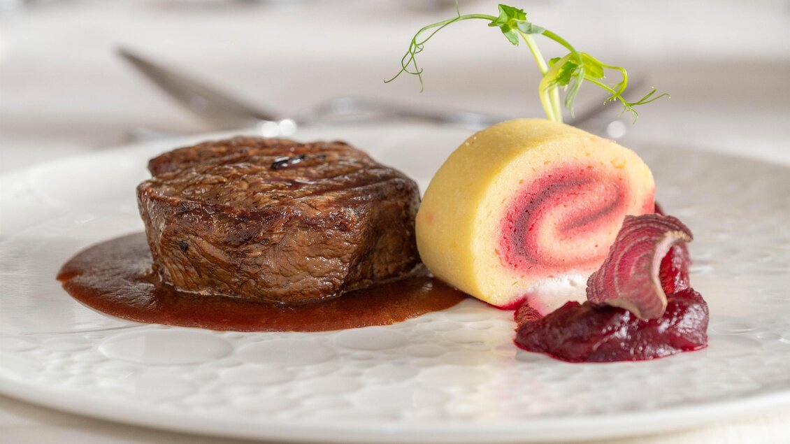 Ein saftiges Steak auf einem eleganten Teller mit einer cremigen Beilage und einer fruchtigen Soße. Das Gericht ist kunstvoll angerichtet und sieht sehr appetitlich aus. | © RETTER Bio-Natur-Resort, Helmut Schweighofer