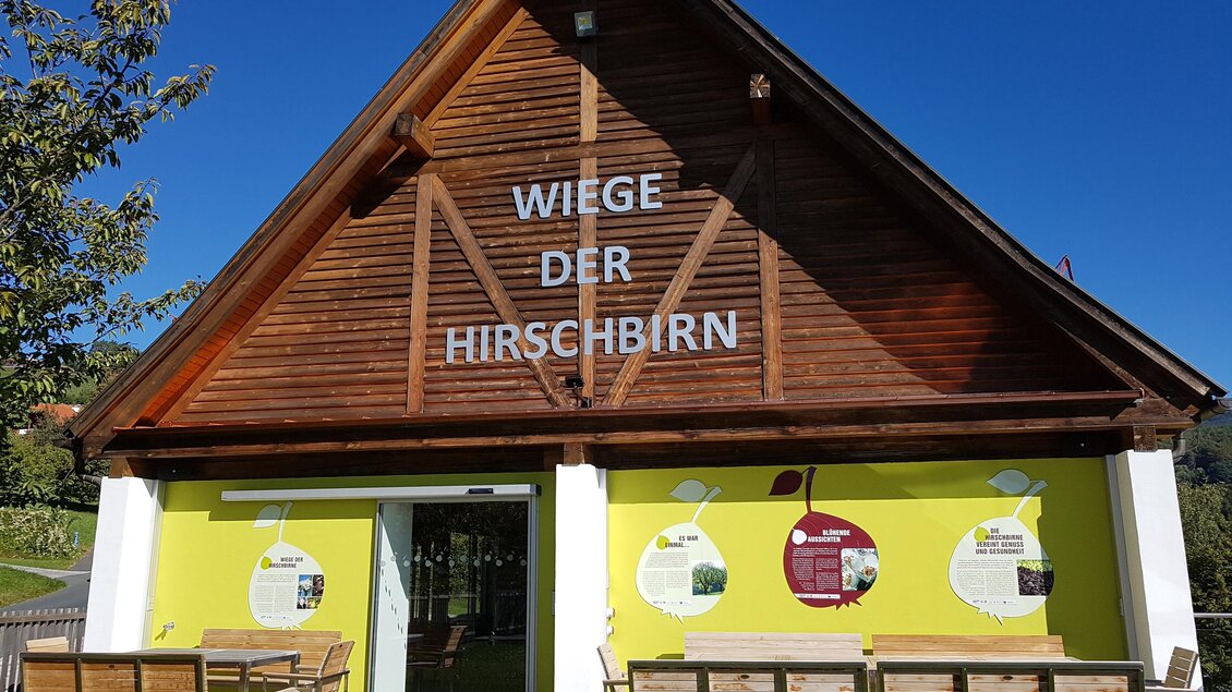 Ein modernes Holzgebäude mit gelben Wänden und einer großen Beschriftung. Vor dem Gebäude stehen Bänke und Tische im Freien. | © Tourismusverband Oststeiermark