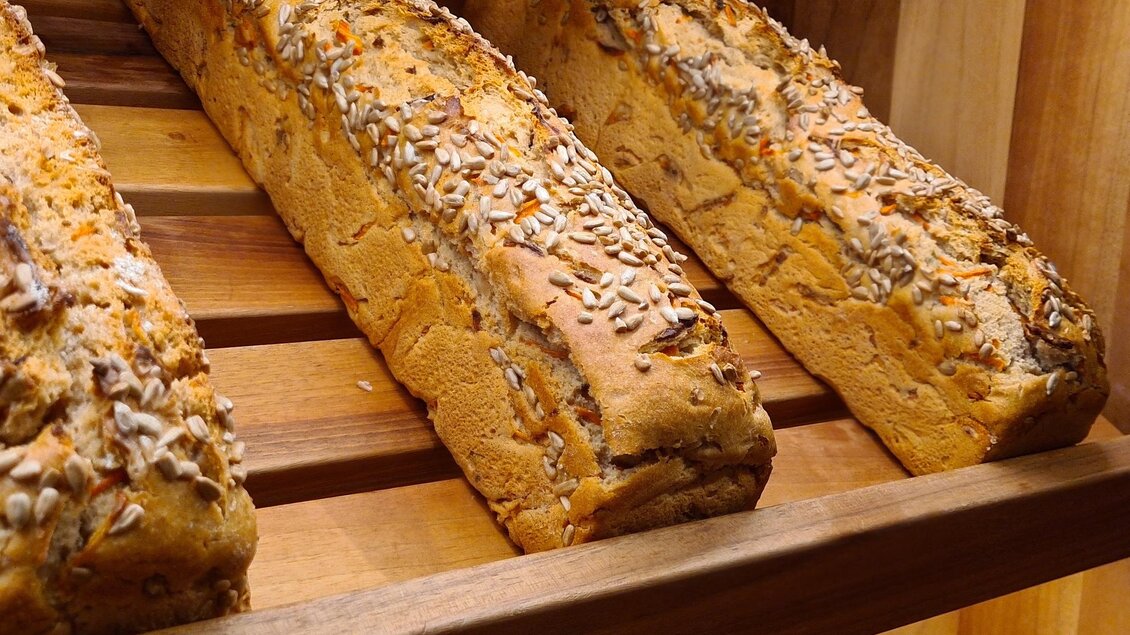 Frisches, knuspriges Brot mit Saaten auf einem Holzregal. Die Laibe sind goldbraun und appetitlich präsentiert. | © Tourismusverband Oststeiermark