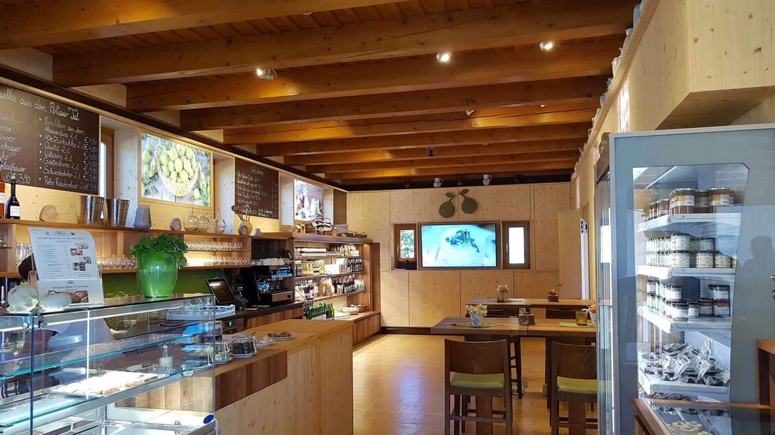 Ein gemütliches Café mit Holzdecken und warmem Licht. Es gibt eine Vitrine mit verschiedenen Leckereien und einen Bereich mit Tischen zum Sitzen. | © Tourismusverband Oststeiermark