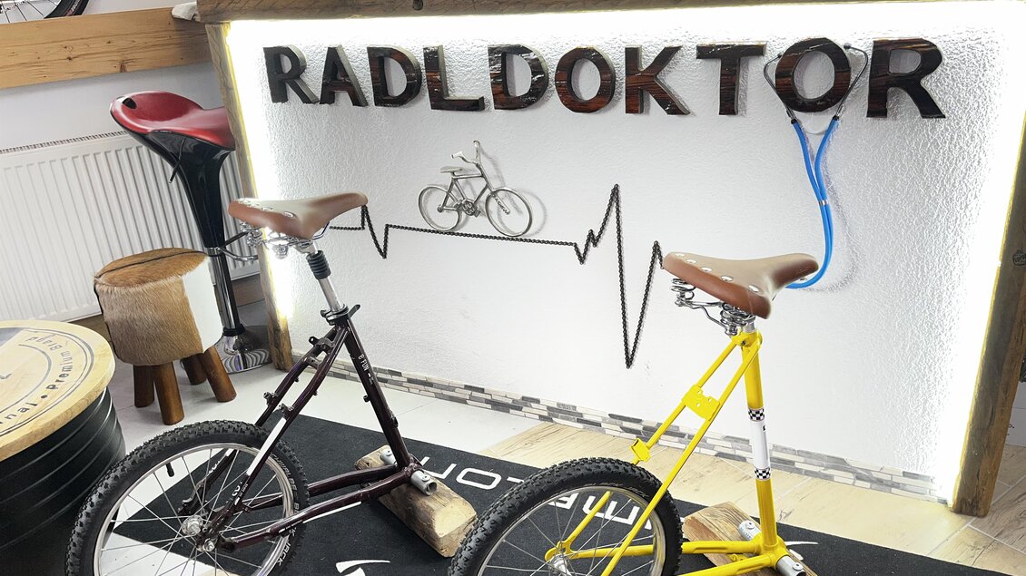 Zwei Fahrräder stehen vor einem Thekenbereich mit dem Schriftzug "RADLDOKTOR". Der Raum hat eine moderne und einladende Atmosphäre. | © Radldoktor
