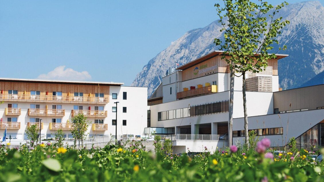 <p>Das Moderne Aldiana Club Hotel mit Holzakzenten, umgeben von grünen Wiesen und blühenden Blumen. Im Hintergrund ist der beeindruckende Grimming sichtbar.</p> | © Karin Ackermann