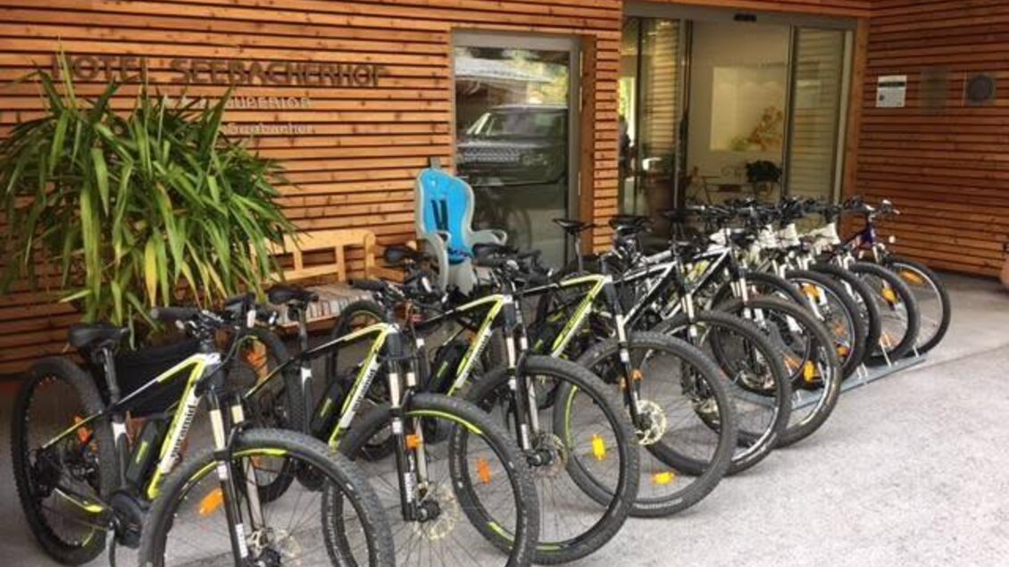 Radverleih Hotel Seebacherhof Eine Reihe von Mountainbikes steht vor einem Holzgebäude. Im Hintergrund sind Pflanzen und ein Stuhl zu sehen. | © Mario Seebacher