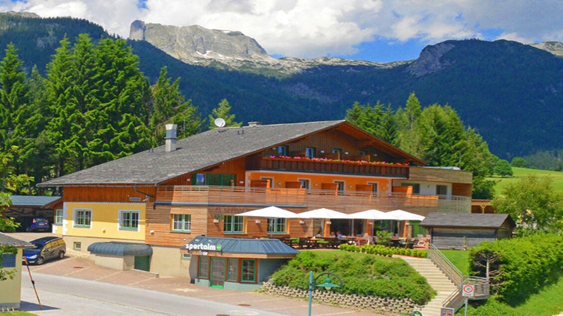 Ein charmantes Gebäude im Alpenstil mit einem Restaurant und Sonnenschirmen. Im Hintergrund erheben sich majestätische Berge und grüne Bäume. | © Hotel Seebacherhof