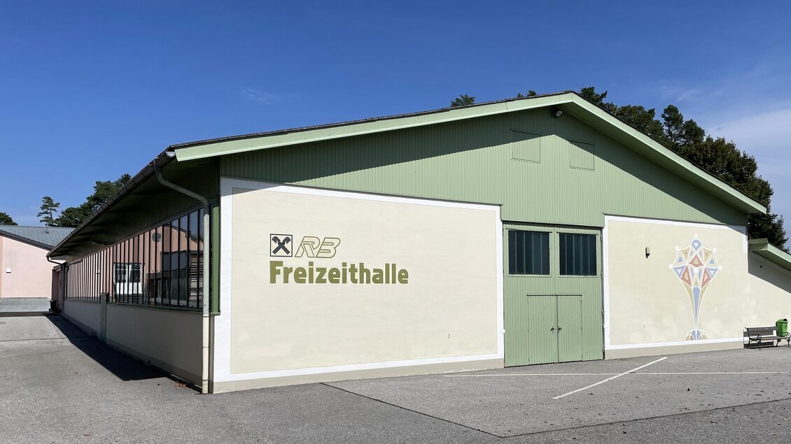 <p>Ein lichtdurchflutetes Gebäude mit dem Schriftzug "Freizeithalle". Die Fassade ist in sanften Farben gehalten und der Himmel ist klar. Die Veranstaltungshalle befindet sich in St. Magdalena.</p> | © Gemeinde Buch-St. Magdalena