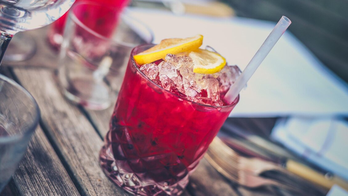 Ein roter Cocktail mit Eis und Zitronenscheiben. Der Drink steht auf einem Holztisch und wirkt erfrischend. | © Pixabay