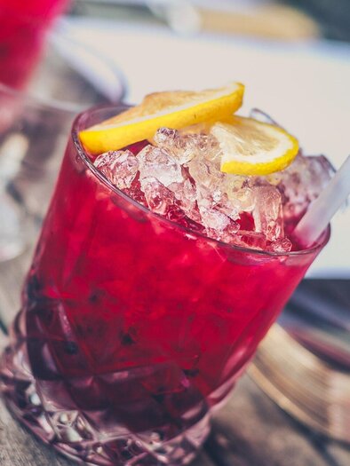 Ein roter Cocktail mit Eis und Zitronenscheiben. Der Drink steht auf einem Holztisch und wirkt erfrischend. | © Pixabay