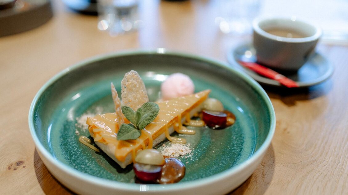 Ein kunstvoll angerichtetes Dessert auf einem grünen Teller. Es besteht aus einer Schicht mit Karamell, dazu frische Früchte und eine kleine Kugel Eis. | © Obersberger