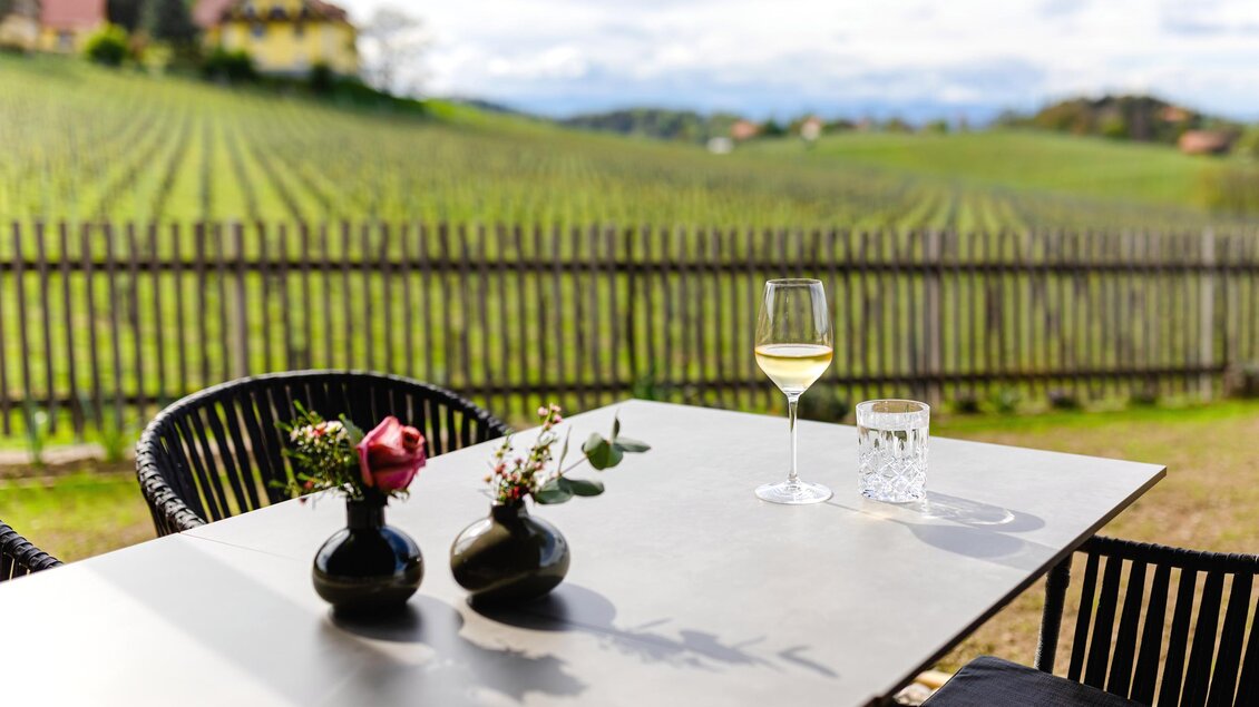 Ein schöner Tisch auf einer Terrasse mit Blick auf Weinreben. Auf dem Tisch stehen zwei Vasen mit Blumen und ein Glas Wein. | © Ratscher Landhaus