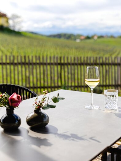 Ein schöner Tisch auf einer Terrasse mit Blick auf Weinreben. Auf dem Tisch stehen zwei Vasen mit Blumen und ein Glas Wein. | © Ratscher Landhaus