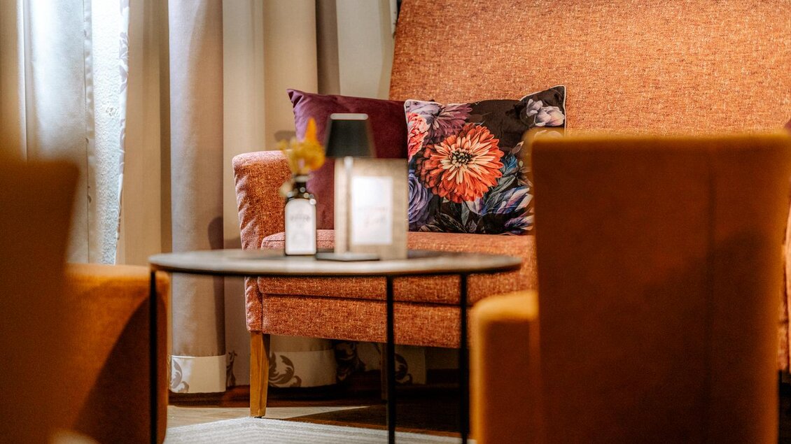 Ein gemütlicher Couchbereich mit einem orangefarbenen Sofa und einem Tisch. Auf dem Tisch stehen eine Lampe und eine dekorative Flasche. Weinbar-Feeling | © Obernberger