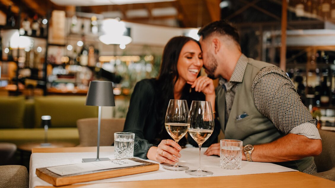 Ein romantisches Pärchen in einer stilvollen Bar. Ein Paar genießt ihre Zeit zusammen mit Gläsern Wein und einem Lächeln. | © Karin Bergmann