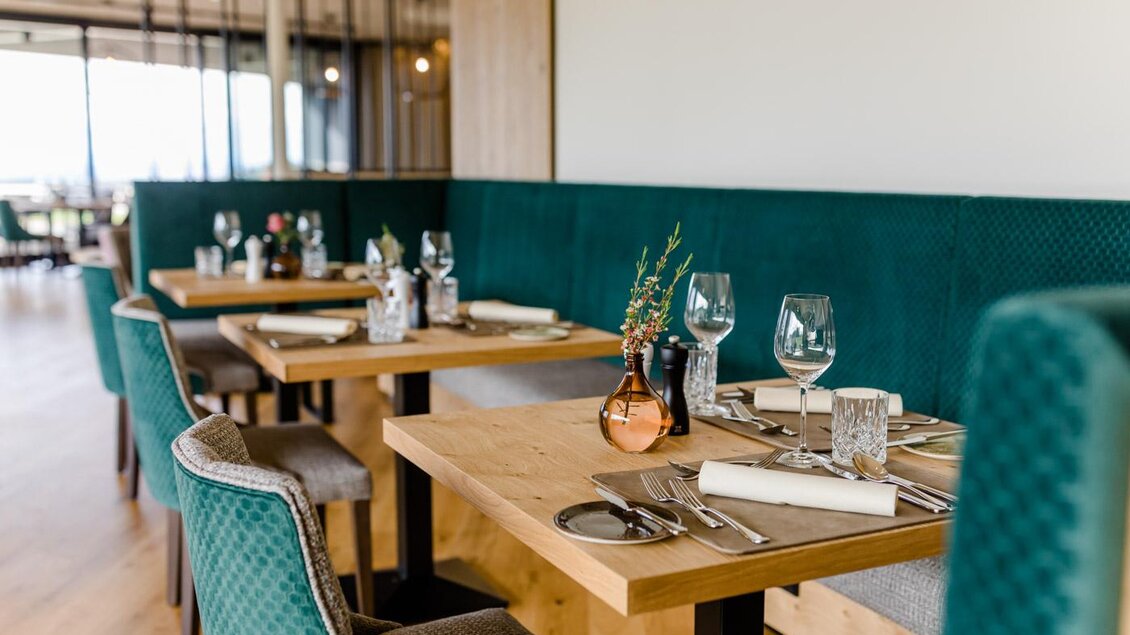 Ein stilvolles Restaurant mit holzfarbenen Tischen und grünen Sitzbänken. Die Tische sind elegant gedeckt mit Gläsern und Besteck. | © Karin Bergmann