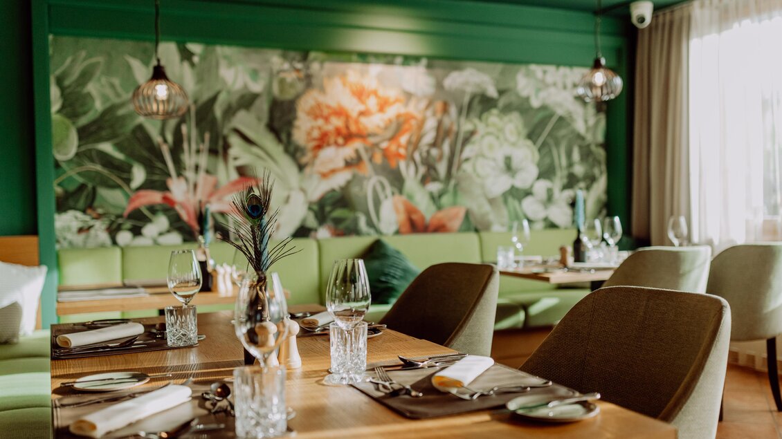 Ein elegantes Restaurant mit einer grünen Wanddekoration und einer großen Pflanzenmalerei. Tische sind schön gedeckt und bieten eine einladende Atmosphäre. Der Grüne Salon. | © Karin Bergmann