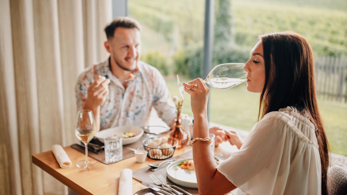 Ein romantisches Abendessen mit einem Paar am Tisch. Sie genießen köstliches Essen und trinken Wein, während sie die Aussicht auf die Weinberge genießen.