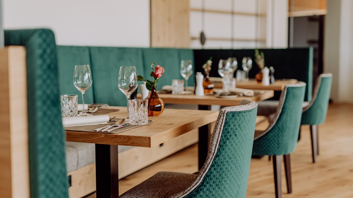 Ein elegantes Restaurant mit Holz-Esstischen und grünen Stühlen. Die Tische sind für Gäste vorbereitet, mit Gläsern und kleinen Blumen dekoriert. | © Ratscher Landhaus