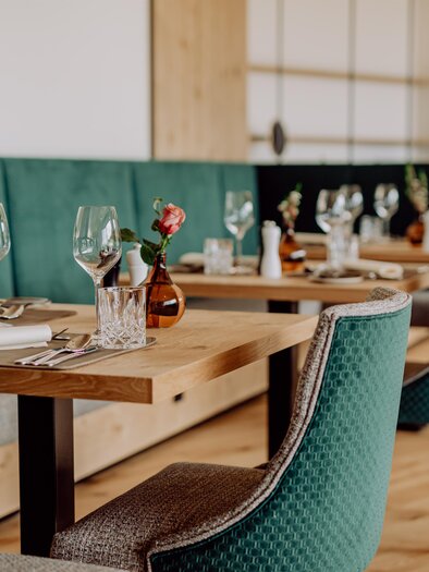 An elegant restaurant with wooden dining tables and green chairs. The tables are set for guests, decorated with glasses and small flowers. | © Ratscher Landhaus