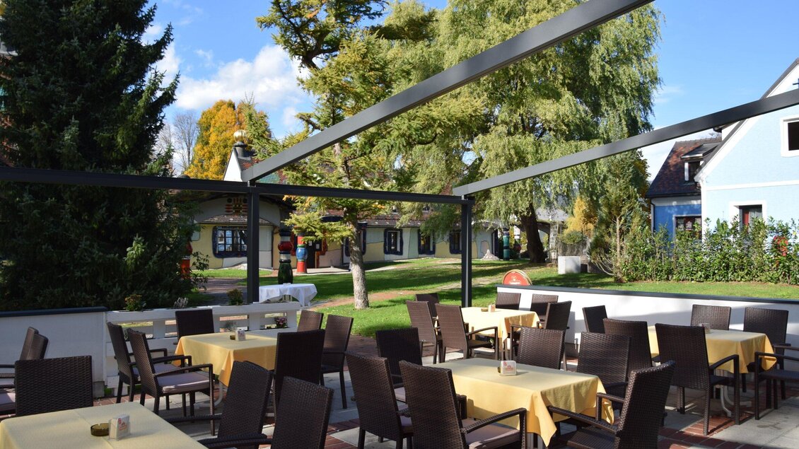Blick auf die Terrasse des Ratskellers in Bärnbach, mit Tischen und Stühlen unter einer modernen Pergola, umgeben von grünen Bäumen und einem gepflegten Garten. | © Ratskeller-Kienzl