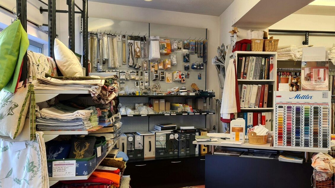 Ein gemütlicher Stoffladen mit Regalen voller bunter Stoffe und Nähzubehör. An der Wand hängen verschiedene Materialien und Angebote. | © Stephanie Bor