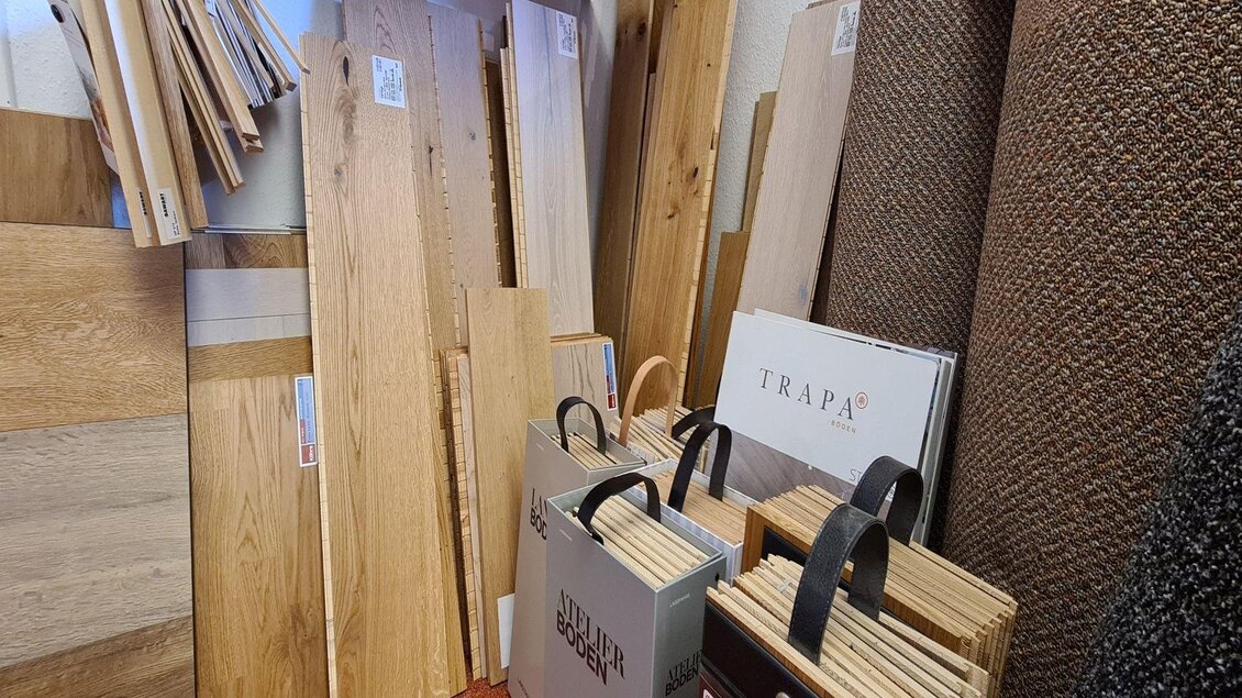 Eine Auswahl an Holzplatten und Bodenbelägen steht in einem Raum. Im Vordergrund sind Musterkarten in Tragetaschen sichtbar. | © Stephanie Bor