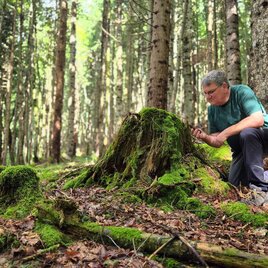 Jürgen Freller im Wald knieend vor einem bemoosten Baumstumpf. Hier genießt er die Kraft der Natur mit allen Sinnen. | © Jürgen Freller