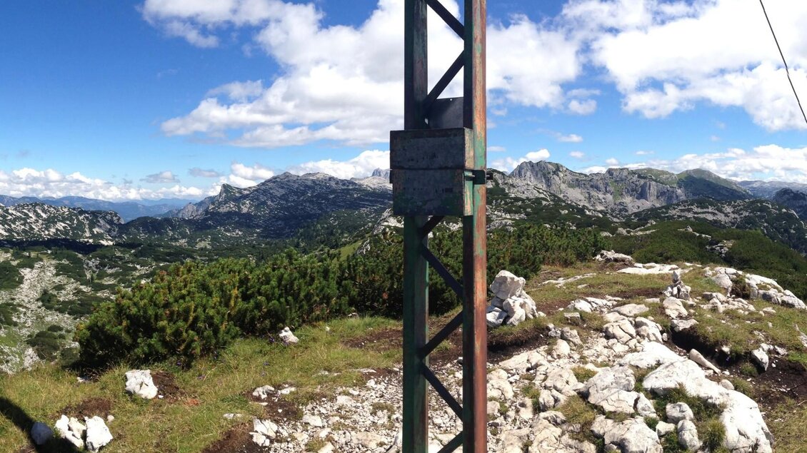 Eine Berglandschaft mit grünen Wiesen und felsigen Erhebungen. Im Hintergrund sind hohe Berge und ein blauer Himmel mit weißen Wolken zu sehen. | © Bettina Scheck