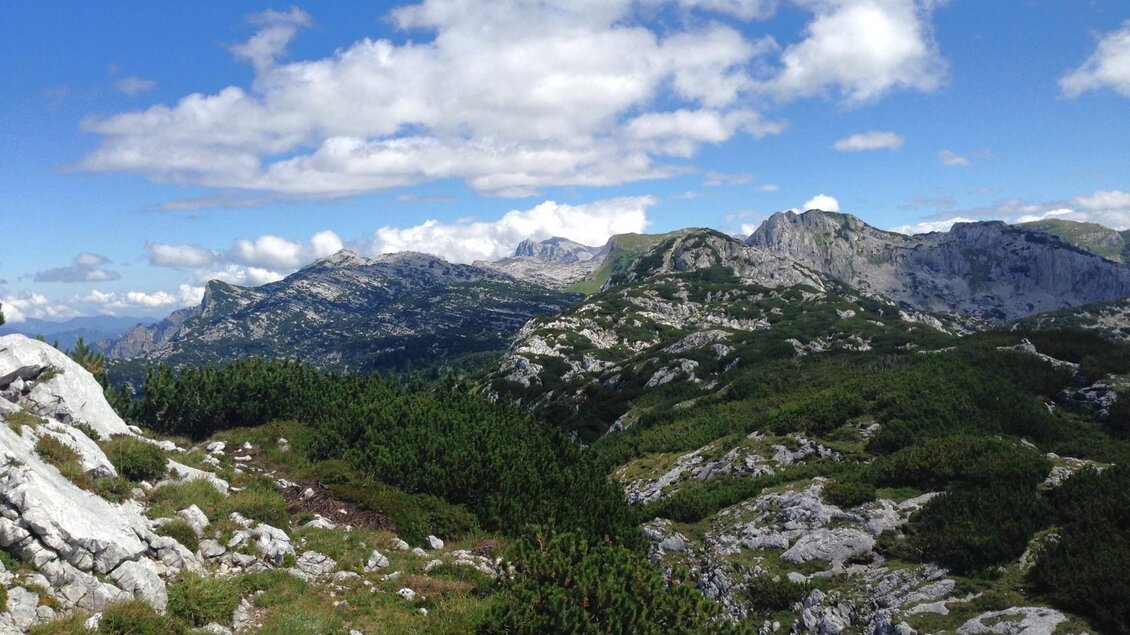 Eine beeindruckende Berglandschaft mit grünen Wäldern und steilen Felsen. Der Himmel ist blau mit einigen Wolken. | © Bettina Scheck