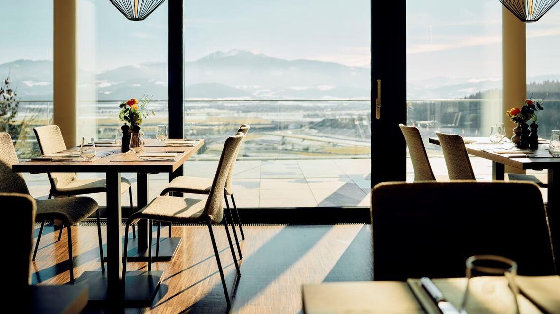 Ein elegantes Restaurant mit modernen Tischen und Stühlen. Durch große Fenster hat man einen schönen Blick auf die Berge und die Landschaft. | © Tauroa GmbH