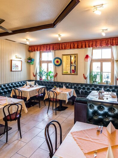 Ein gemütliches Restaurant mit dunkelgrünen Polstermöbeln und hellen Tischdecken. Die Wände sind dekoriert und es gibt mehrere Pflanzen im Raum. | © Stephan Friesinger
