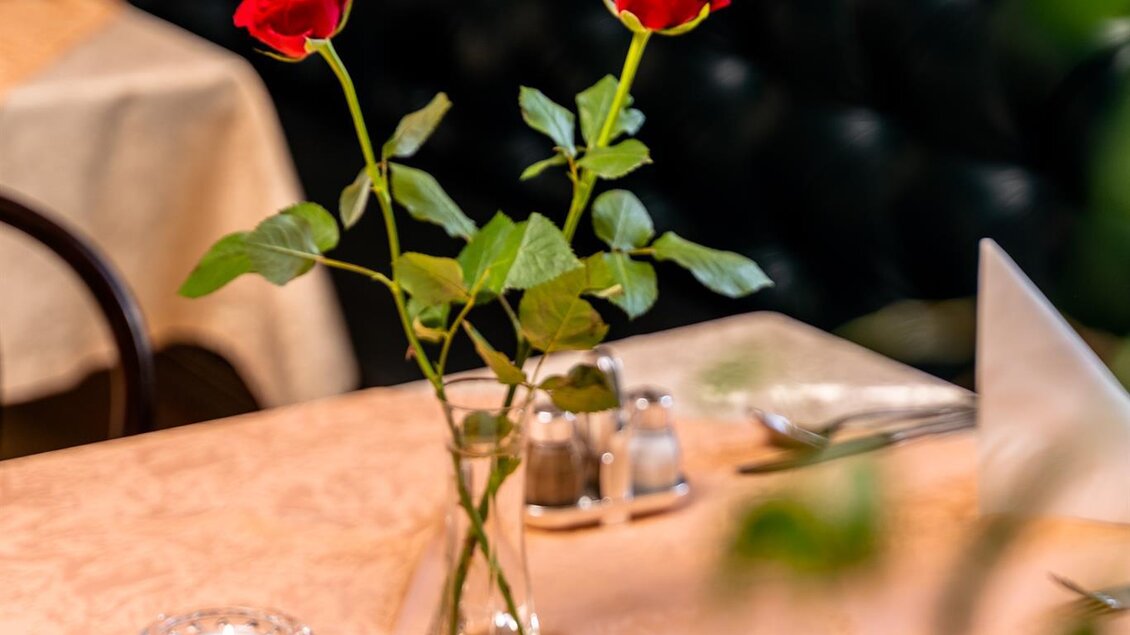 Ein schön angerichteter Teller mit einem Gericht und frischem Gemüse liegt auf einem Tisch. Darüber steht eine rote Rose in einer Vase, die eine romantische Atmosphäre schafft. | © Stephan Friesinger